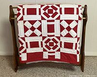 Quilt displayed folded on pine quilt stand, showing bold geometric red and white pattern.