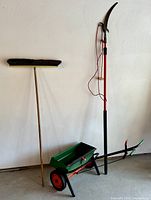 Full view of the seeder, trimmer, and broom leaned against a wall showing their size and condition