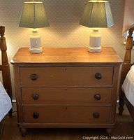 Front view of the worn rustic maple dresser between two beds, two lamps visible on top.