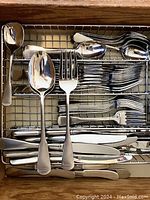 Flatware set with forks, spoons, knives and spoons arranged in tray, showing satin stainless finish and classic Colonial Boston pattern handles.