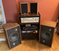 Overview of pine cabinet holding stereo receiver and CD player, with small speakers on top and large speakers on floor
