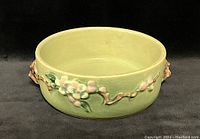 Front view of round melon green pottery bowl with raised apple blossom flowers and branches in white, pink, and green.