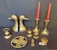 Full view of all brass items showing candlesticks, bookends, trivet, candle holders, dinner bell, stamp roller, and small bells.
