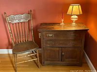 Photo showing an oak spindle chair with leaf motif backrest next to an oak washstand with electric lamp and glass candlestick on top.