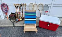 Full view of croquet set with six mallets, six balls, metal wickets; tennis rackets, paddle tennis racket, portable lawn seat, and Coleman cooler