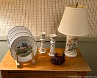 Set of four Villeroy & Boch plates arranged on a wooden stand next to floral candlesticks, lamp, and cranberry glass turkey figurine on a table.