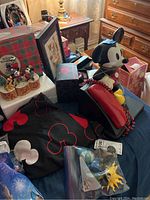Photo showing Mickey Mouse telephone, Mickey's Winter Wonderland figurines, black fabric with Mickey pattern, other Disney collectibles on table.