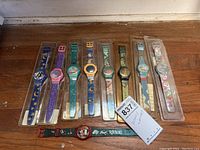 Top view showing eight Disney watches in plastic packaging and one loose watch laid out in a row