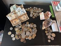 Coins and bills spread on a black surface, showing a variety of sizes and conditions.