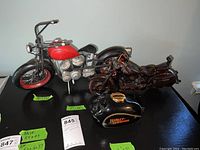 Wide view of the three items on a black surface: two Harley Davidson motorcycle models and a ceramic piggy bank with Harley Davidson branding.