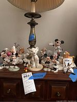 Photo showing assorted Lenox Disney figurines on a wooden surface under a lamp, featuring Mickey Mouse, Minnie Mouse, Lion King character, and others.