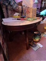 Oval white marble top table with dark wooden legs placed indoors with various items on top and underneath removed from sale.