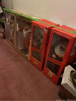 Four boxed Christmas motion figurines arranged in a row showing original packaging and box designs, set on carpeted floor.