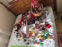 Full view of assorted holiday ornaments and collectibles laid out on a bed including basket with baubles, figurines, and decorations.