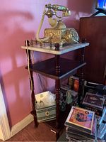 Side view of wooden telephone table with white marble top and rotary phone on top, visible missing drawer pull and lower shelf storage.