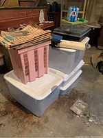 Six plastic storage bins with lids, pink crate, desk telephone, desk accessories, and wallets stacked together in a basement.