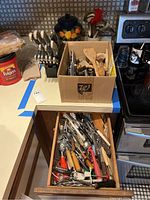 Photo showing assorted kitchen utensils in a box on the counter, next to a knife block and stove.