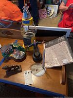 Photo of the wooden table displaying all items including Wizard of Oz gumball machine, singing man music box, cast lion statue, and moon landing newspaper.