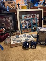 Photo showing various framed Yankees prints, Derek Jeter bobblehead box, checkerboard set, baseball, plush dice with NY logo, watch, and shot glass all arranged on floor.