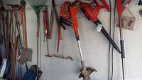 Full view of hanging yard tools: shovels, rakes, cutters, trimmer, blower, hedge cutter.
