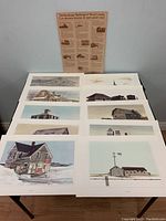 Ten rural Canadian building prints laid out on a table showing various barns and houses, unframed.