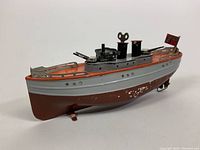 Side view of tin ship showing red and gray painted hull with paint wear.