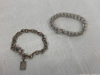 Two 925 silver bracelets laid flat showing overall condition, one with a charm and toggle clasp, one with woven chain style.