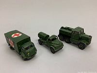 Front and side view of three vintage military toy trucks: ambulance, water tanker, and recovery tractor aligned on a white background.