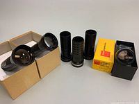Six vintage projection lenses including Kodak Ektanar zoom lens in original yellow box and other black tubular lenses.