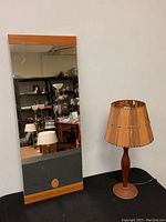 Photo showing the full mirror with teak wood frame and the wooden table lamp with shade on black surface.