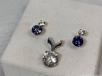 Pair of stud earrings and pendant displayed on white textured surface, showing front view of stones and design