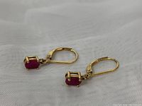 Pair of earrings laid flat showing front view of ruby drops and leverback closures