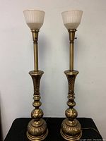 Pair of tall brass torchiere lamps with detailed carved bases and milk glass shades.