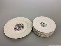 Set of one large 13-inch serving plate and nine 9-inch dinner plates showing white textured porcelain with central floral designs.
