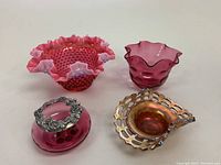 Three pink hobnail scalloped glass bowls with one featuring a silver floral lid, alongside a marigold carnival glass bowl with hobnail pattern and lattice rim.
