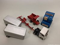 Photo of vintage Linemar Benjamin Franklin savings coin bank with die-cast toy vehicles: white cab semi-truck with silver trailer, red dump truck bed, and another silver trailer piece, arranged closely on plain background.