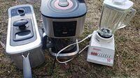 Photo showing all three appliances side by side outdoors on grass: the deep fryer on left, the coffee maker in center, and the blender on right.