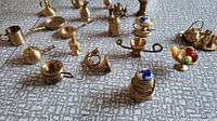 Wide view of brass miniatures including pans, cups, pot, horn and basket with glass fruit on a textured surface