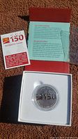 Silver medallion displayed in white case inside a red box with CIBC 150th anniversary card and informational insert.
