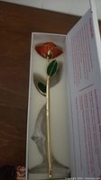 Photo of electroplated rose with collector box insert showing red rose with green leaves on gold stem in white box.