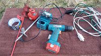All items arranged on a brown cloth outdoors showing drill, batteries, charger, ground stakes, extension cords.