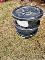 Three black plastic 5-gallon feed tubs stacked showing top lids with star reinforcement and surface wear.