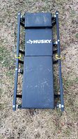 Top view of folded collapsible trolley creeper showing Husky logo on padded black surface and metal frame.