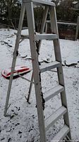 Photo of the aluminum step ladder showing side with steps and supporting braces outdoors on snow ground.
