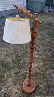 Full height image of the vintage wood floor lamp standing on grass with a cream pleated lampshade attached and a power cord visible.