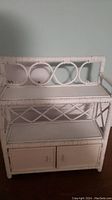 Photo of white wicker shelf with decorative circular back design, two shelves, and double-door storage cabinet at the bottom.
