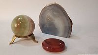 Polished agate sphere with metal stand, flat oval agate piece, and upright agate half-slice.