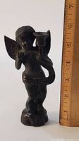 Front view of bronze cherub candelabrum standing next to ruler showing height approx 6 inches.
