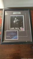 Full view of framed Elvis Presley memorabilia including photo and stamp, seen on wooden surface.