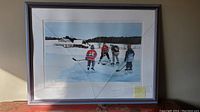 Framed print showing four children playing hockey outdoors in a winter landscape, cracked glass is visible in the frame.